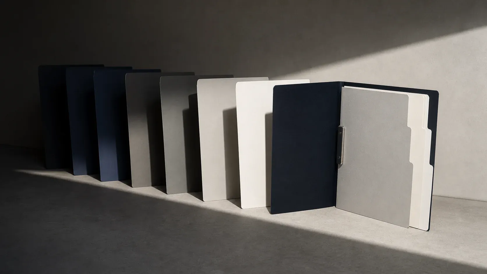 A measured sequence of dark and pale archival folders crossing from shadow into light
